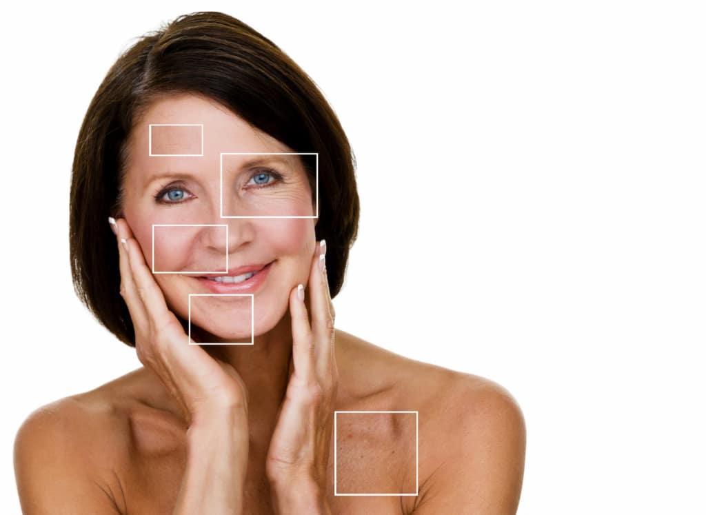 headshot of shirtless woman holding face with white square outlines against solid white background