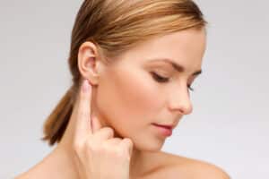 Woman pointing to her nice ears after cosmetic ear surgery in Denver, CO