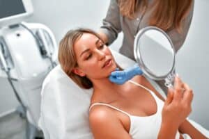 Woman looking in the mirror with doctor after FaceTite procedure in Denver, CO