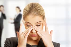 Woman in an office holding her eyes due to blepharospasm in Denver, CO